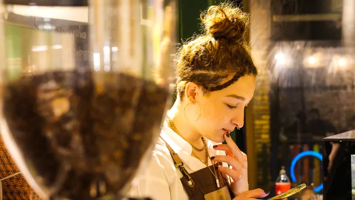 Barista revisando mensajes de clientes en su celular en la cafetería