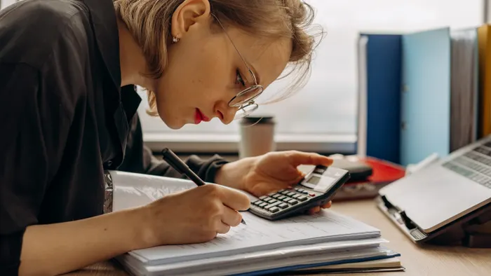 Mujer revisando documentos y usando una calculadora en su escritorio