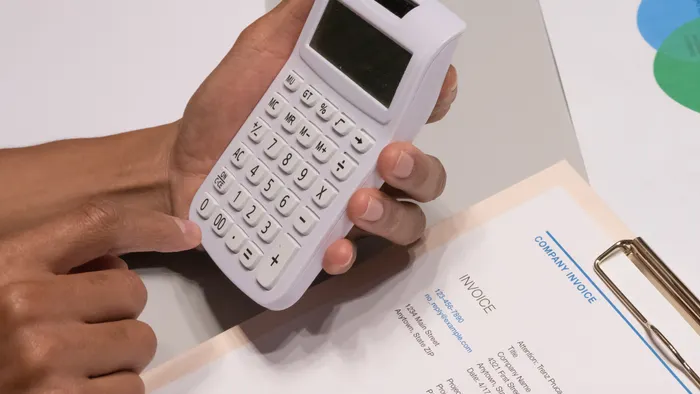 Manos usando una calculadora junto a una factura impresa sobre un escritorio