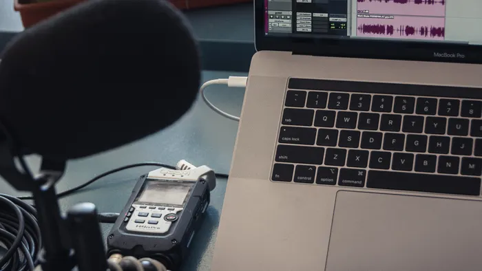 Micrófono y grabadora de audio junto a una laptop que muestra la onda de una grabación