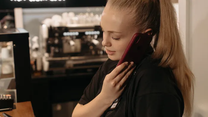 Trabajadora de una cafetería atendiendo una llamada con el teléfono, detrás del mostrador