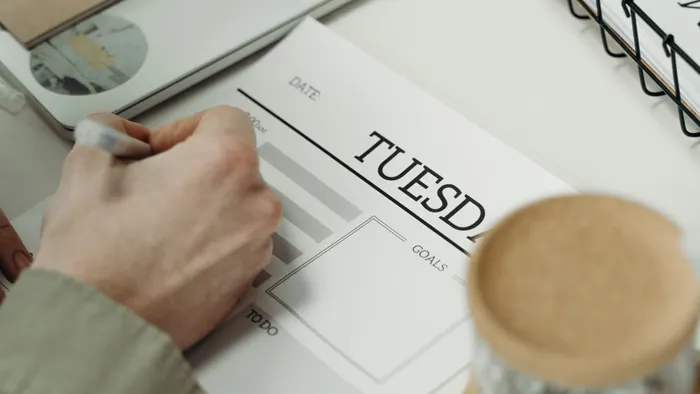 Mano escribiendo en una agenda con secciones de fecha, objetivos y tareas pendientes
