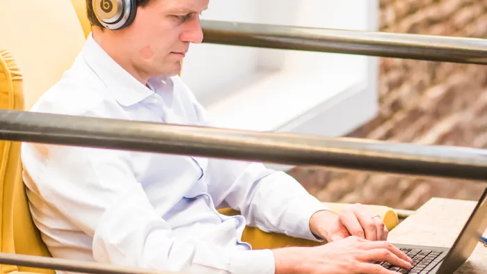 Hombre con audífonos escribiendo en una laptop mientras escucha una grabación en la oficina