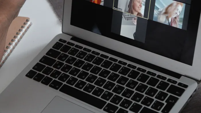 Laptop mostrando una videollamada grupal, junto a una libreta sobre la mesa